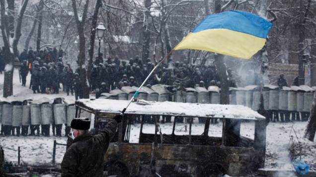 Ucraniano abana bandeira em frente a tropa de choque durante confrontos com manifestantes pró-Europa, em Kiev