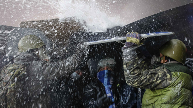 Manifestantes pró-Europa se protegem de jato dàgua lançado pela policia, em Kiev