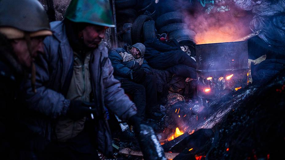 Manifestantes anti-governo se aquecem em um fogueira perto de uma barricada, em Kiev, na Ucrânia
