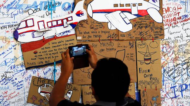 <p>Homem tira foto de desenhos de aviões em homenagem ao voo desaparecido em mural no aeroporto de Kuala Lumpur na Malásia</p>