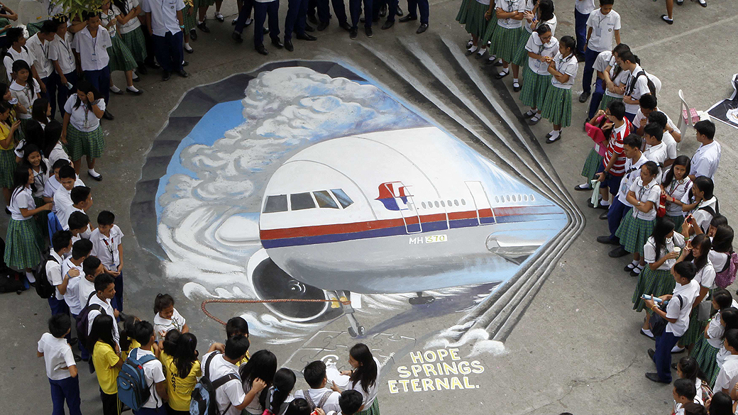 Estudantes se reúnem em torno de obra de arte tridimensional, baseada no voo 370 da Malaysia Airlines, desaparecido desde 8 de março, pintada em Makati (Filipinas)