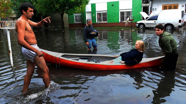 Vizinhos ajudam mulher com uma canoa em rua inundada em La Plata, sudoeste de Buenos Aires, na Argentina