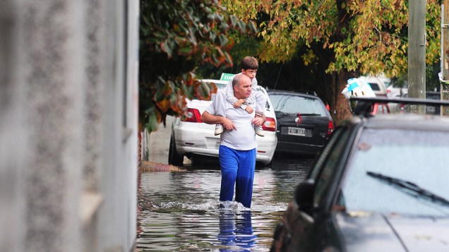 Homem carrega menino nas costas em rua inundada em La Plata, na Argentina