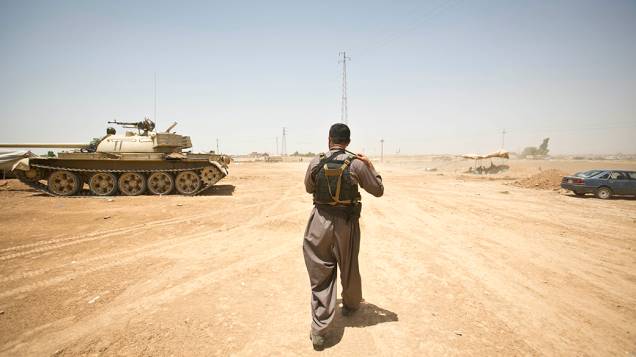 Na aldeia iraquiana de Basheer, membro das forças curdas passa por um tanque durante uma pausa nos combates contra militantes sunitas liderados pelo Estado Islâmico do Iraque e do Levante (ISIL)