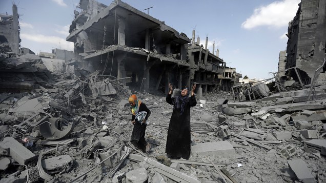 Mulher caminha em meio a edifícios destruídos por bombardeios israelenses no distrito de Beit Hanoun na Faixa de Gaza durante trégua humanitária
