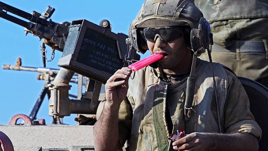 Soldado israelense se refresca tomando um picolé sobre um tanque a caminho da Faixa de Gaza