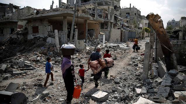 Famílias palestinas caminham entre casas destuídas por mísseis israelenses, na Faixa de Gaza