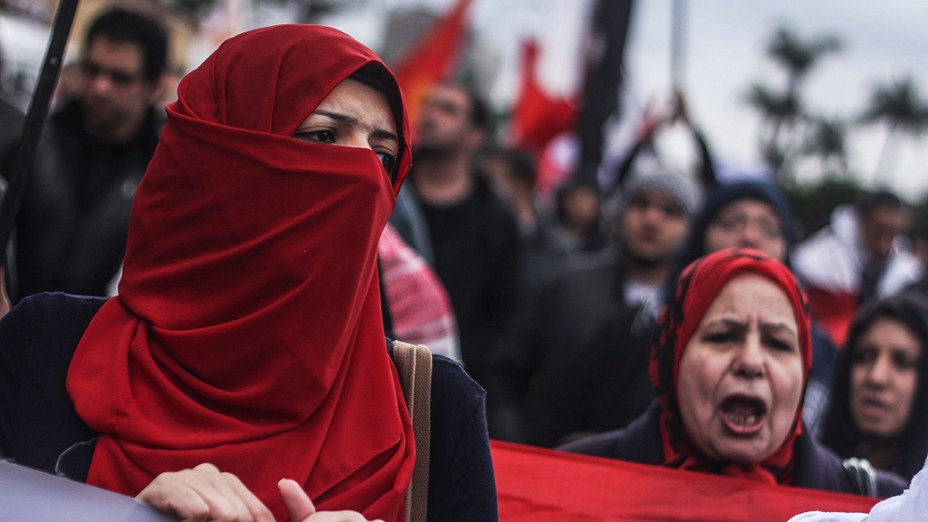 Uma mulher em um hijab está na frente de um tanque.