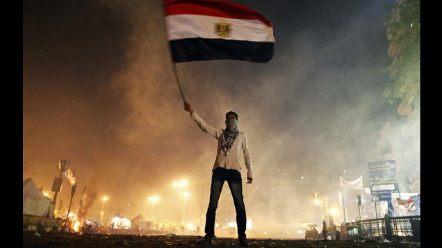 Manifestante conduz a bandeira egípcia em meio a fumaça de bombas de gás lacrimogênio durante protestos na praça Tahrir no Cairo, no segundo aniversário da revolta que derrubou o presidente Hosni Mubarak