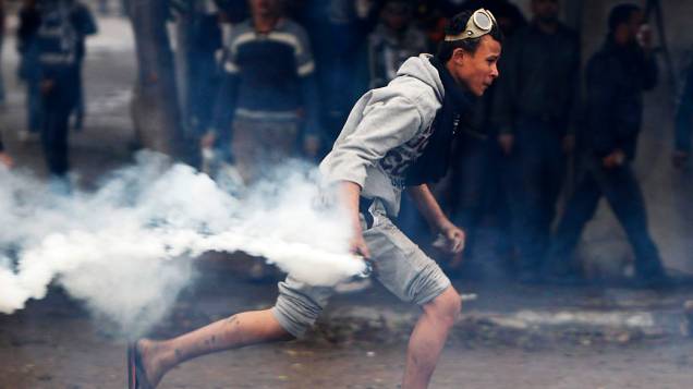 Manifestante se prepara para lançar bomba de gás lacrimogêneo de volta para a polícia durante confrontos na Praça Tahrir, Cairo