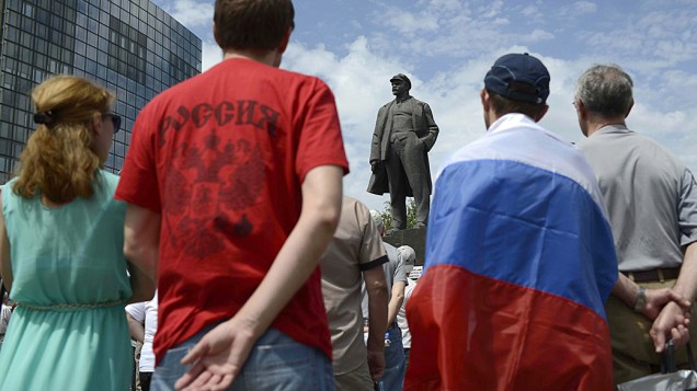 Manifestante vestindo uma bandeira russa se ​​reúne em frente a uma estátua de Lenin durante uma manifestação anti-eleições no centro da cidade de Donetsk
