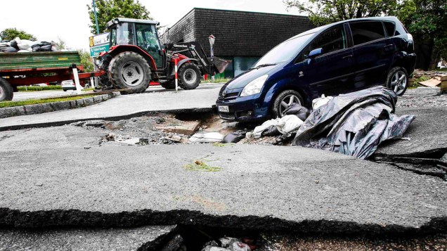 Um carro fica preso dentro de um buraco, em uma rodovia danificada pela chuva e enchentes, na Áustria