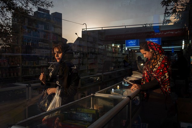 Rua de um bairro comercial é refletida na janela de uma farmácia na cidade de Teerã, no Irã