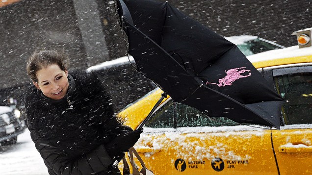 <p>Mulher tenta agarrar o seu guarda-chuva durante uma forte nevasca em Nova York </p>