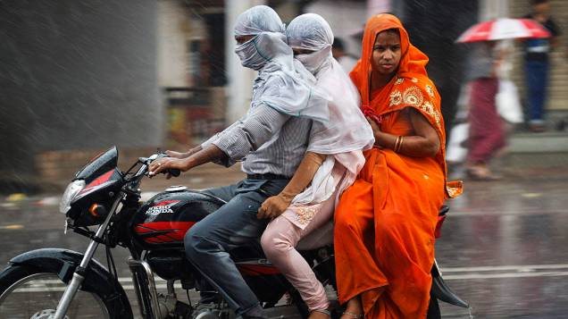 Homem monta uma motocicleta  junto com sua família durante uma chuva forte na cidade de Allahabad, norte da Índia