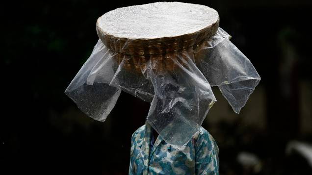 Um vendedor de peixe carrega sua cesta na cabeça coberta com plástico enquanto caminha durante a chuva em Mumbai, Índia