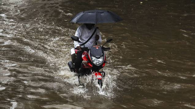 Homem passa por rua alagada com uma moto em Mumbai, na Índia