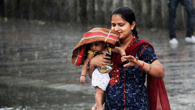 Mulher carrega seu filho durante chuva pesada na cidade de Chandigarh, na Índia