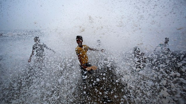 Meninos brincam em um paredão onde as ondas quebram durante uma chuva de monção em Mumbai, na Índia