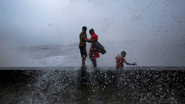 Casal se abraça enquanto ondas quebram sobre uma parede durante a temporada de monções da Índia, em Mumbai