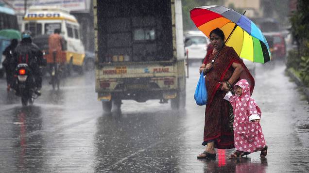 Mulher e sua filha atravessam uma estrada durante chuva de monções em Mumbai, na Índia