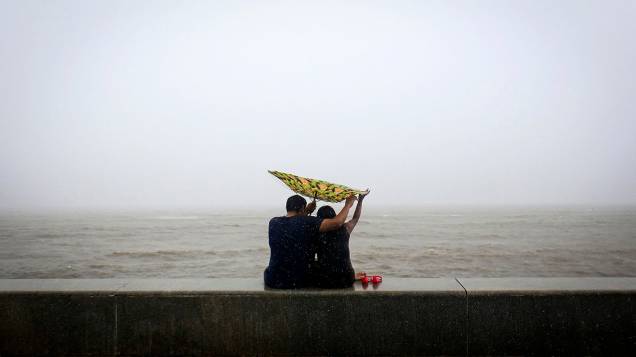 Casal tenta segurar o guarda-chuva virado do avesso em frente em uma praia na costa do Mar Arábico, em Mumbai, na Índia