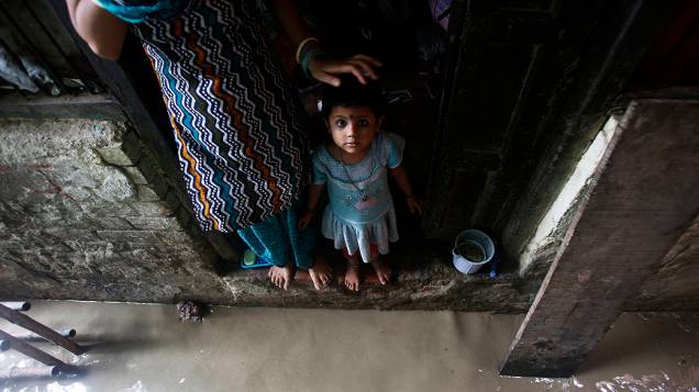 Criança olha enquanto da porta de sua casa inundada devido à cheia do rio Yamuna, na Índia