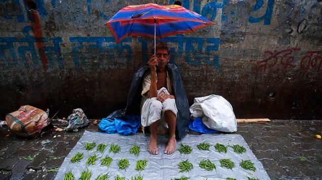 Vendedor de legumes se protege da chuva sentado sobre a lona de um mercado durante as chuvas de monções em Mumbai, na Índia