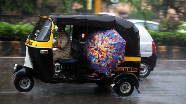 Pessoas se protegem das chuvas dentro de um riquixá em Mumbai, na Índia