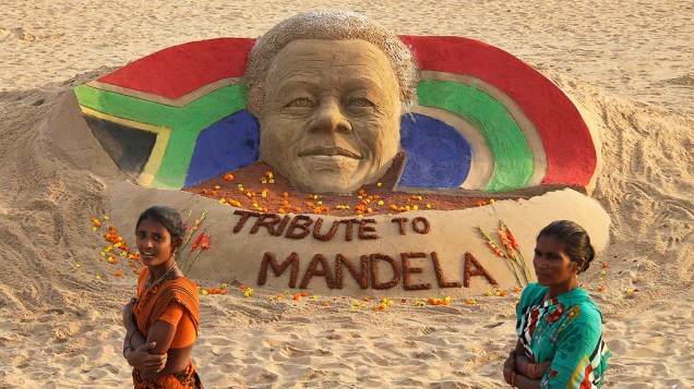 mulheres passam por uma escultura de areia em homenagem ao ex-presidente Sul-Africano Nelson Mandela criada pelo artista Sudarshan Pattnaik, em Puri, na Índia