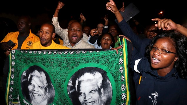Sul-africanos cantam em frente à casa de Nelson Mandela em Johannesburgo, para homenagear o ex-presidente, morto nesta quinta-feira (05), aos 95 anos
