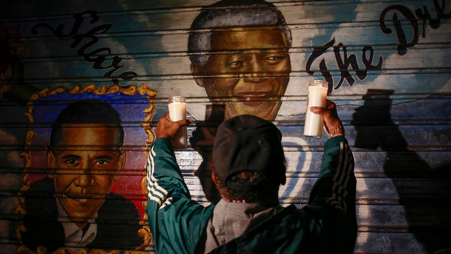 Em Nova York, homem segura velas em frente a um mural com a imagem do ex-presidente sul-africano Nelson Mandela, e do presidente dos Estados Unidos, Barack Obama