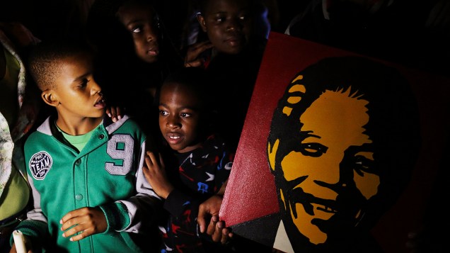 Crianças seguram cartaz com a imagem de Nelson Mandela  em frente à casa onde ele morava, em Johannesburgo