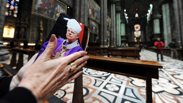 Mulher faz orações com uma fotografia do cardeal Angelo Scola na Catedral de Milão, Itália
