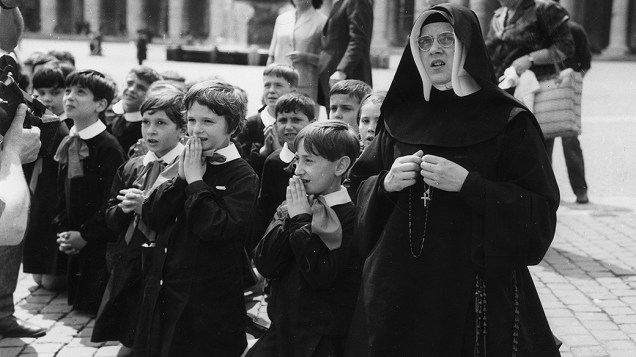 1963 - Uma freira com algumas crianças se ajoelham em oração na Praça de São Pedro à espera de notícias do papa João XXIII, que estava gravemente doente