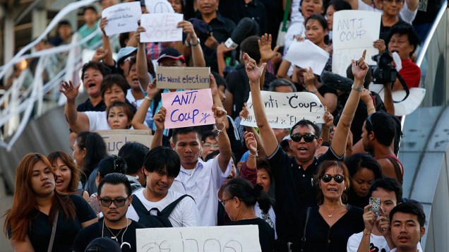 Dezenas de manifestantes gritam palavras de ordem e mostram cartazes durante um protesto contra o regime militar no centro da cidade de Bangcoc, um dia após o exército tailandês tomar o poder em um golpe de Estado