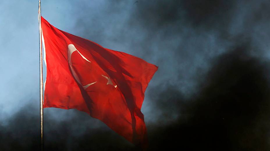 Bandeira da Turquia sob fumaça preta da queima da barricada feita pelos manifestantes em Istambul, na Turquia