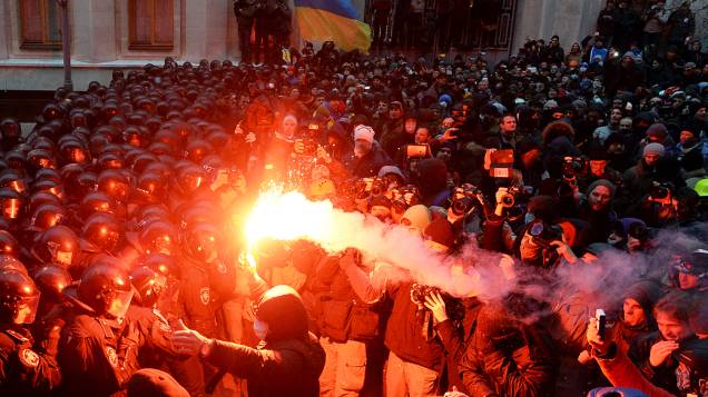 Manifestante segura um sinalizador na frente de policiais de choque durante confrontos perto do escritório presidencial, em Kiev, na Ucrânia
