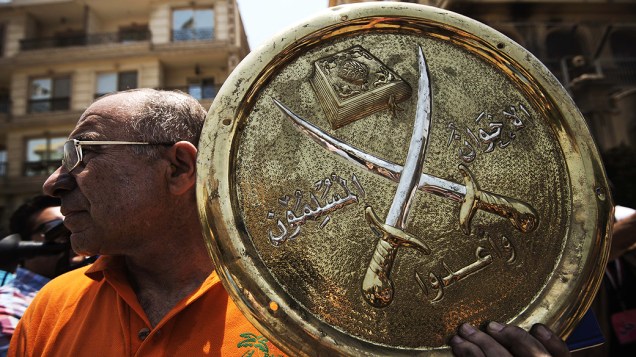 Homem segura uma placa com o emblema da Irmandade Muçulmana que foi retirada da sede do partido incendiada no distrito de Moqattam do Cairo, na segunda-feira 1º de julho