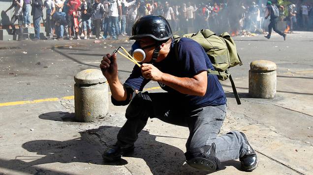 Manifestante usa um estilingue para atigir a polícia durante protesto contra o governo de Nicolás Maduro, em Caracas