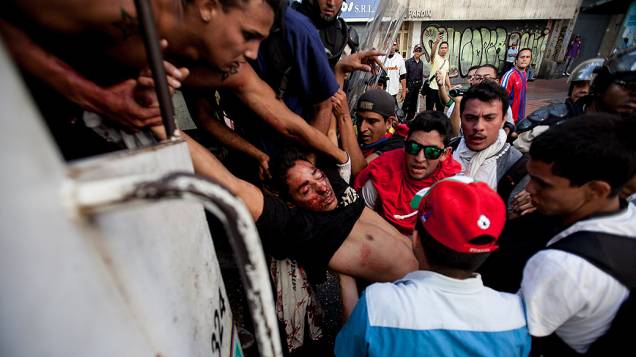 Estudante ferido com um tiro na cabeça é levado por outros manifestantes para o interior de um veículo da polícia em Caracas, Venezuela