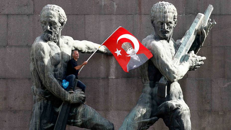 Manifestante segura bandeira da Turquia sentado em um monumento, durante um protesto contra o primeiro-ministro, Tayyip Erdogan e seu Partido AK, em Ancara