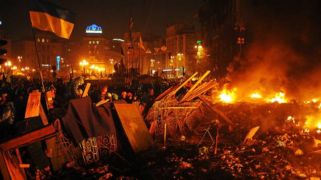 Grupo de manifestantes anti-governo permanece atrás de uma barricada durante confrontos contra a polícia nesta quarta-feira (19), na Praça da Independência, no centro de Kiev