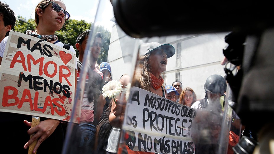 Manifestantes da oposição seguram cartazes em frente a um bloqueio de policiais durante protesto contra o governo do presidente Nicolas Maduro, em Caracas - (17/02/2014)