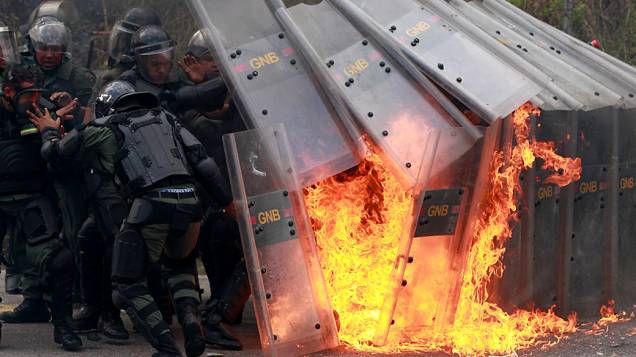 Membros da Guarda Nacional Venezuelana reagem após serem atingidos por um coquetel molotov jogado por estudantes durante confrontos na Universidade Metropolitana de Caracas
