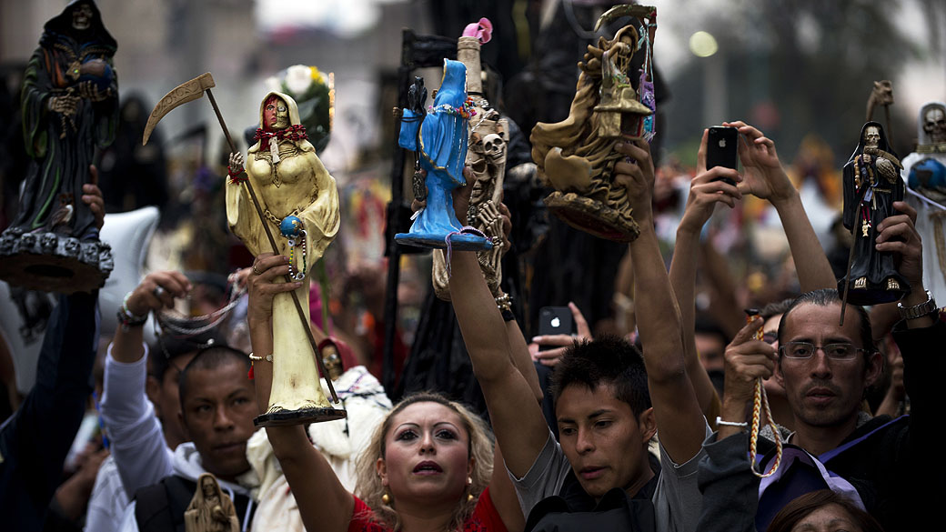 Devotos erguem imagens de Santa Muerte, diante do altar central, pedindo favores durante a celebração principal no mercado de um dos bairros mais perigosos, conhecido como Tepito, no México