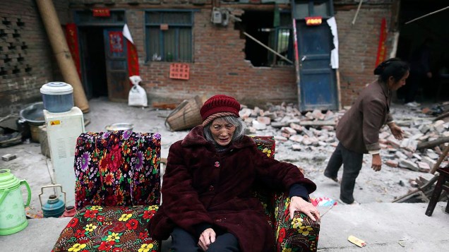 Idosa senta em um sofá na frente de casas destruidas por terremoto na cidade de Taiping Lushan, província de Sichuan, China