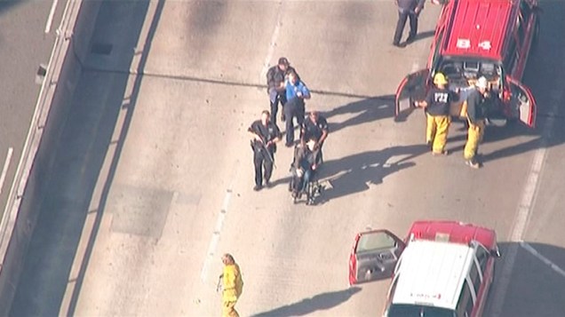 Polícia escolta um homem em uma cadeira de rodas para que ele receba ajuda médica, após tiroteio no Aeroporto Internacional de Los Angeles