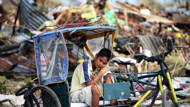 Jovem sobrevivente repousa sobre um triciclo nos destroços causados ​​pelo tufão Haiyan em Tacloban, nas Filipinas