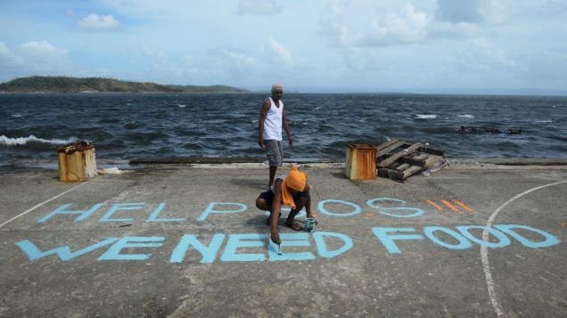 Homem pinta mensagem "SOS Ajuda, Precisamos de comida" em Tacloban, leste da ilha de Leyte, nas Filipinas